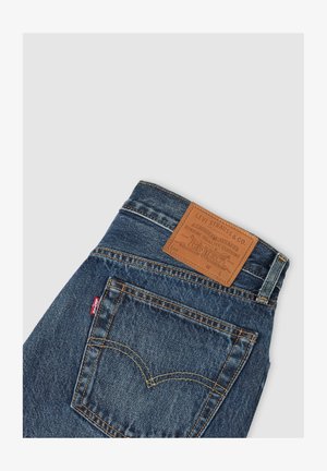 Dunkelblaue Denim-Jeans mit gelben Nähten, ausgestattet mit einem braunen Lederpatch am Bund und einem markanten Design auf der Gesäßtasche.