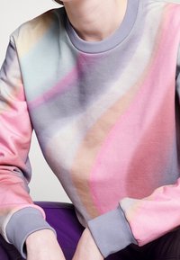 Sudadera con un diseño de remolino en tonos pastel de rosa, morado y azul, confeccionada en un tejido suave con textura, puños acanalados y cuello redondo.
