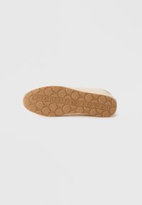 Des chaussures Tommy Hilfiger dotées d'une semelle en caoutchouc avec un motif hexagonal et un logo en relief de couleur beige.