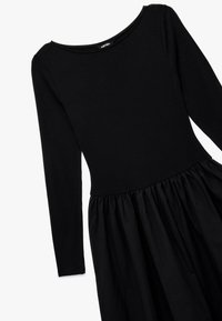 Schwarzes langärmliges Kleid mit rundem Ausschnitt und gerafftem Rock. Hergestellt aus weichem Stoff, mit tailliertem Oberteil und ausgestelltem Saum.