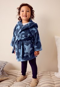 Blå fleecebadekåbe med stjerner, hætte, bælte i taljen og lomme; båret over mørke leggings og lyse hjemmesko; blød tekstur.