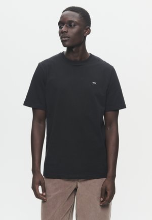 Čierne bavlnené tričko s krátkymi rukávmi a okrúhlym výstrihom, s malým bielym logom na ľavom prsníku. Jednoduchý dizajn, bez vzorov.