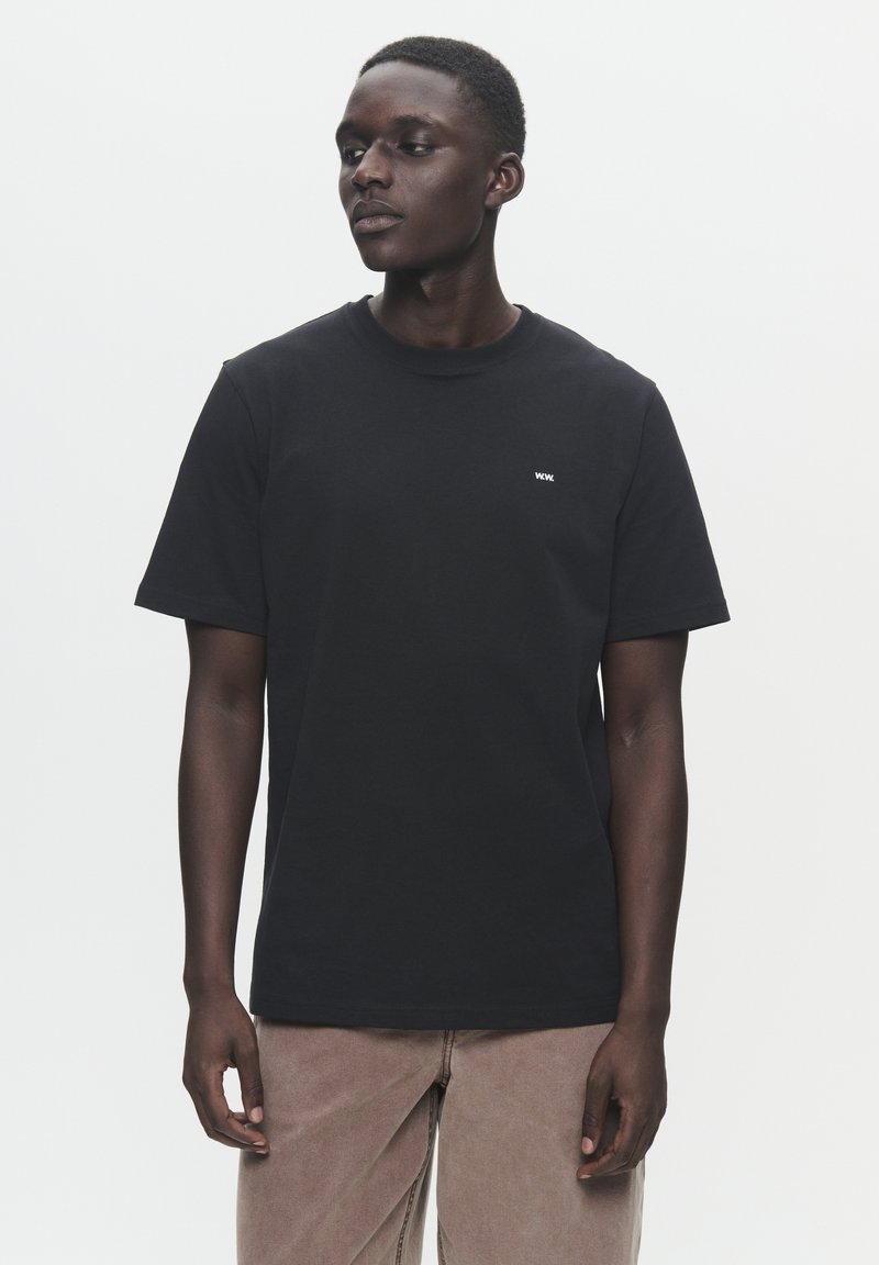 T-shirt de algodão preta com mangas curtas e decote redondo, com um pequeno logótipo branco no lado esquerdo do peito. Design simples, sem padrões.
