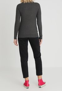 Pull gris côtelé à manches longues, associé à un pantalon noir fuselé et des baskets montantes roses, vu de dos.