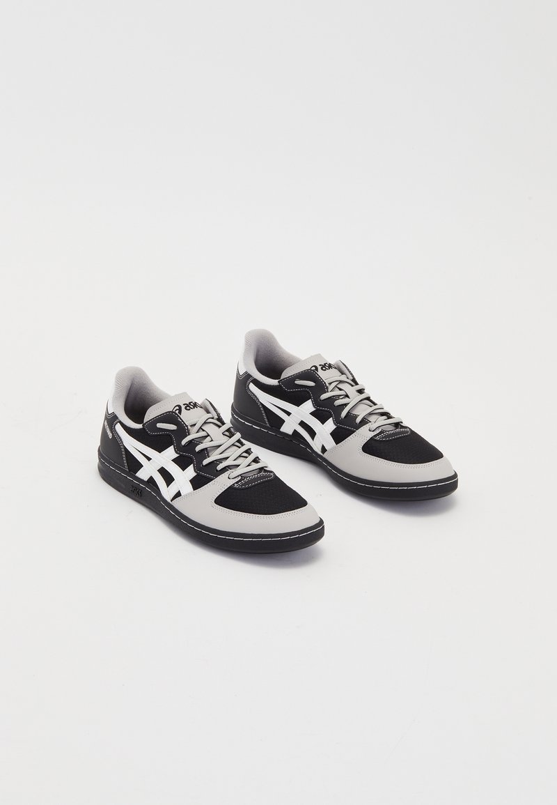 Paire de baskets basses noires et grises avec des bandes blanches marquées et des lacets sur fond blanc.