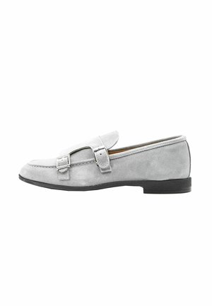 Mocassino in suede grigio con punta rotonda, fascia decorativa con fibbia sul davanti e suola piatta in gomma. Texture liscia e design minimalista.