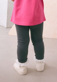 Leggings grises de corte ajustado, combinados con calcetines tobilleros blancos con encaje y zapatillas color crema. Camiseta rosa brillante visible en la parte superior.