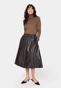 Brauner Rollkragenpullover kombiniert mit einem schwarzen Leder-Midirock, das über einen gerafften, elastischen Bund und eine glatte Textur verfügt.