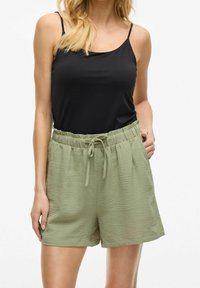 Černý top bez rukávů spárovaný s lehce zelenými texturovanými šortkami se elastickým pasem a nastavitelnou šňůrkou. Hladká látka, volný střih.