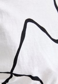 Ligne courbe abstraite noire sur fond de tissu blanc, montrant la texture et les plis du tissu.
