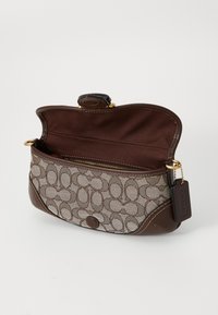 Brown and beige patterned fabric handbag with dark brown leather trim, open flap, gold zipper pocket inside, and a hanging tag on the side.