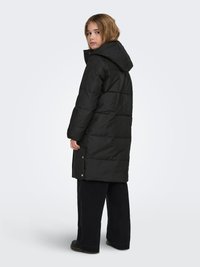 Fekete, kapucnis pufidzseki, steppelt mintával és patentgombos részletekkel az alján. Széles szárú sötét nadrág felett viselve.