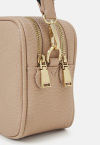Piccola borsa in pelle beige con finitura testurizzata, doppie cerniere dorate e una chiusura metallica dorata. Presenta bordi arrotondati e una tracolla robusta.