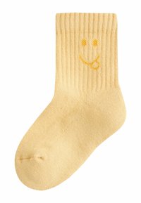 Kollased soonikkudega sokid, millel on naeratava näo kujundus kollase niidiga, pehme tekstuuri ja keha järgiva lõikega.