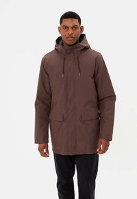 Bruine waterdichte jas met capuchon, lange mouwen, voorzakken en verstelbare trekkoorden. Heeft een gladde, matte textuur.