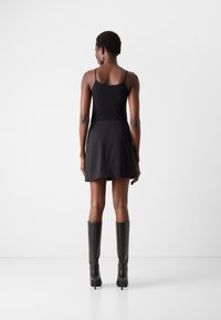 Svart tanktopp kombinert med en svart utsvingt skjørt, supplert med knelange svarte støvler. Jevnt materiale med tettsittende design og minimale sømmer.