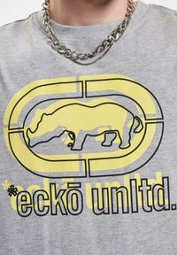 Grijs katoenen t-shirt met een gele afbeelding van een neushoorn met zwarte omlijning, vergezeld van de tekst "eckō unltd." in het zwart.