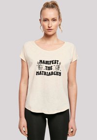 Light beige short-sleeve T-shirt with a scoop neckline and a black graphic print reading "Manifest the Matriarchy." Soft texture.