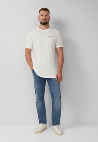 Witte katoenen T-shirt met korte mouwen, voorzien van een kleine zwarte print. Gecombineerd met lichtblauwe spijkerbroek en witte sneakers.