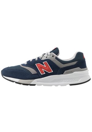 Marineblauwe en grijze New Balance sneaker met rood "N"-logo, witte tussenzool en zwarte buitenzool, van opzij getoond op witte achtergrond.