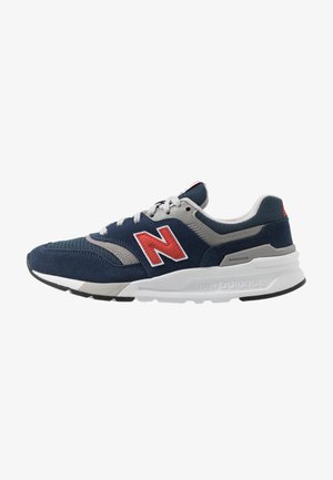 Granatowo-szary but sportowy New Balance z czerwonym logo "N", białą środkową częścią podeszwy i czarną zewnętrzną podeszwą, pokazany z boku na białym tle.