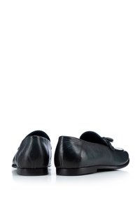 Mocasines de cuero negro con textura suave, punta afilada y detalle de lazo decorativo en la parte superior. Suela delgada de goma.
