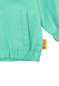 Svetle zelená, hladká látková bunda s elastickými manžetami, malou kapsou a žlutou etiketou s logem medvídka.