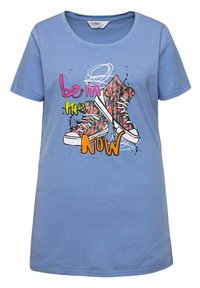 Camiseta de algodón azul claro con un gráfico de zapatillas coloridas y el texto "está en el AHORA" en rosa brillante y verde. Manga corta.