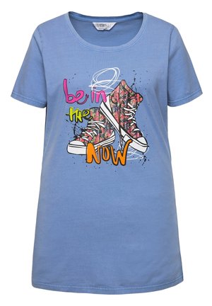 T-shirt in cotone azzurro chiaro con una grafica di sneakers colorate e il testo "essere nel QUI e ORA" in rosa brillante e verde. Maniche corte.