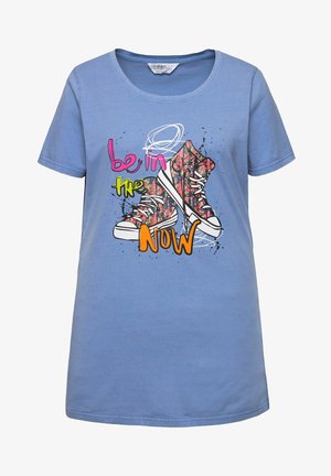 Camiseta de algodón azul claro con un gráfico de zapatillas coloridas y el texto "está en el AHORA" en rosa brillante y verde. Manga corta.