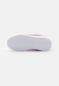 Baskets Nike avec une semelle en caoutchouc blanc arborant un motif en chevrons, des accents roses et une tige en textile lisse.