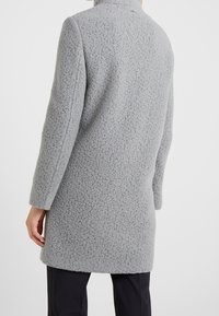 Grå ullkappa med en texturerad yta, rak skärning, långa ärmar och hög krage, med rena linjer och inga synliga knäppningar.