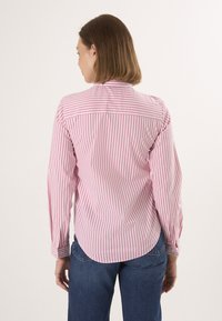 Chemise à manches longues rayée en coton rose et blanc. Caractéristiques : col à boutons, fentes latérales et poignets avec fermetures à boutons.