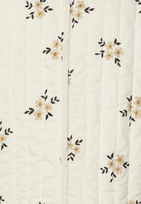 Biancheria da letto trapuntata con sfondo bianco, caratterizzata da piccoli motivi floreali beige e neri, superficie strutturata con linee di cucitura verticali.