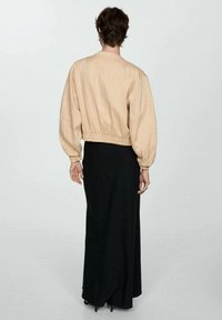 Beżowa krótka kurtka z balonowymi rękawami i elastycznym pasem, zestawiona z długą czarną spódnicą, prezentująca minimalistyczny design.