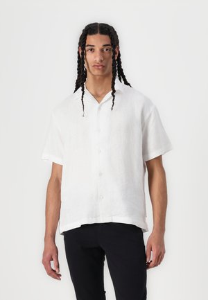 Chemise blanche en lin à manches courtes avec une fermeture à boutons sur le devant, col, et coupe décontractée ; texture lisse et apparence légère.