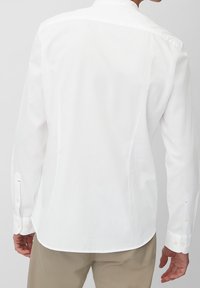 Vit långärmad skjorta, knäppdesign med skräddarsydd passform. Har en rundad nederkant och knäppte manschetter med subtila detaljer. Slät textur.