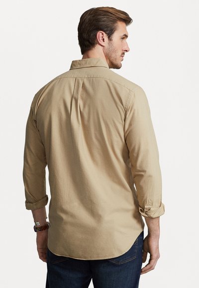 Beige långärmad skjorta, slim fit, mjukt bomullstyg, knappad krage, rundad nederkant, uppvikta ärmar, bärs med mörkblå jeans.