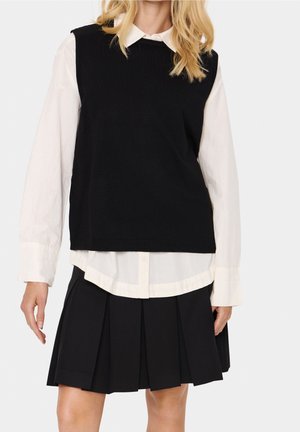 Black knitted sleeveless sweater over a white button-up shirt, paired with a pleated black skirt. Simple design with a clean, layered look.