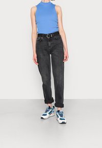 Blå ärmlös topp, svarta jeans med uppvikta muddar och blå-vita sneakers. Materialet verkar slätt; jeansen har en lätt blekt struktur.