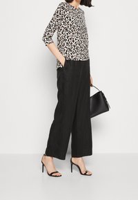 Blouse met luipaardprint en driekwartmouwen, gecombineerd met zwarte wijde broek en zwarte hoge hakken, en een zwarte handtas.