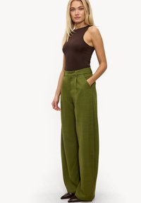 Body marron sans manches associé à un pantalon vert à jambes larges et taille haute, avec des poches latérales et un tissu texturé.