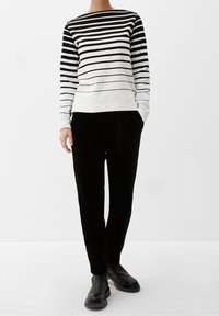 Randig svartvit långärmad tröja med vid halsringning, som matchas med svarta kordbyxor och kraftiga svarta stövlar.