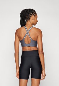 Sujetador deportivo gris de corte atlético con tirantes entrecruzados y detalle de logo, combinado con pantalones cortos negros de cintura alta, con textura suave y diseño ajustado.