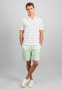 Stripete polo skjorte i hvit og marineblå, parret med mintgrønne shorts. Casual bomullsstoff, avslappet passform. Fottøy: hvite sneakers.