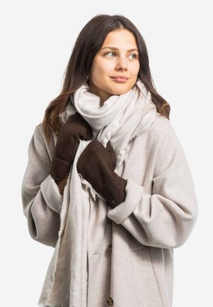 Brown suede mittens are held against a light gray scarf, worn with a loose-fitting, beige coat featuring a button detail.