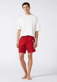 Shorts de bain rouges avec une taille élastique et un cordon de serrage. Chemise blanche à manches courtes. Tissu lisse. Design minimaliste, sans motifs visibles.