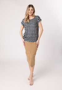 Blusa blu con motivo giallo, vestibilità morbida, maniche corte. Gonna a tubino beige, lunghezza al ginocchio, texture liscia. Modella che indossa sandali bianchi con tacco.