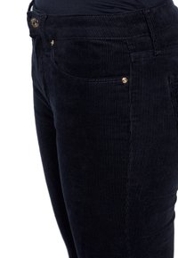 Pantalons en velours côtelé bleu marine foncé avec une texture côtelée. Équipés de détails en métal doré sur les poches et la ceinture, soulignant les lignes verticales du tissu.
