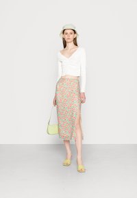 Camisola cropped de manga longa branca com detalhe franzido, saia midi com padrão floral em verde e vermelho, chapéu de balde verde e bolsa em verde claro.